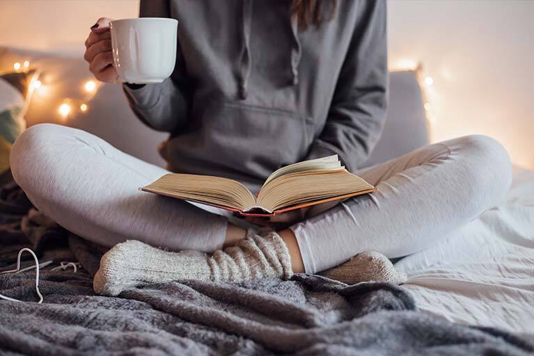 Frau liest ein Buch im Schneidersitz mit Tasse in der Hand