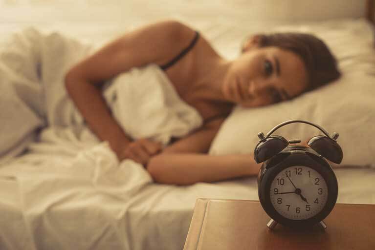 Frau blickt im Bett auf Wecker: Schlaflos